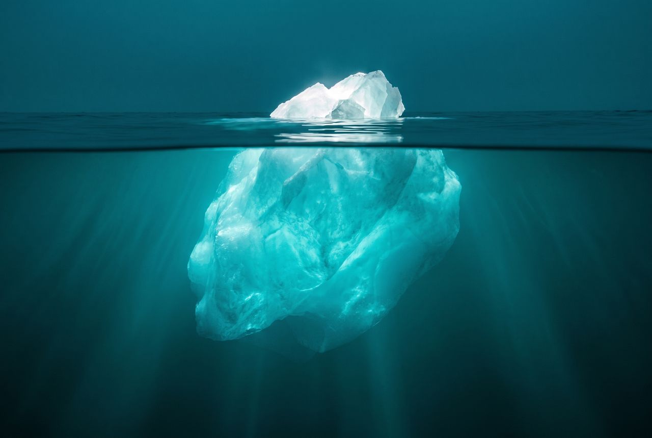 An iceberg at the waterline: a small tip above, a vast glowing mass below